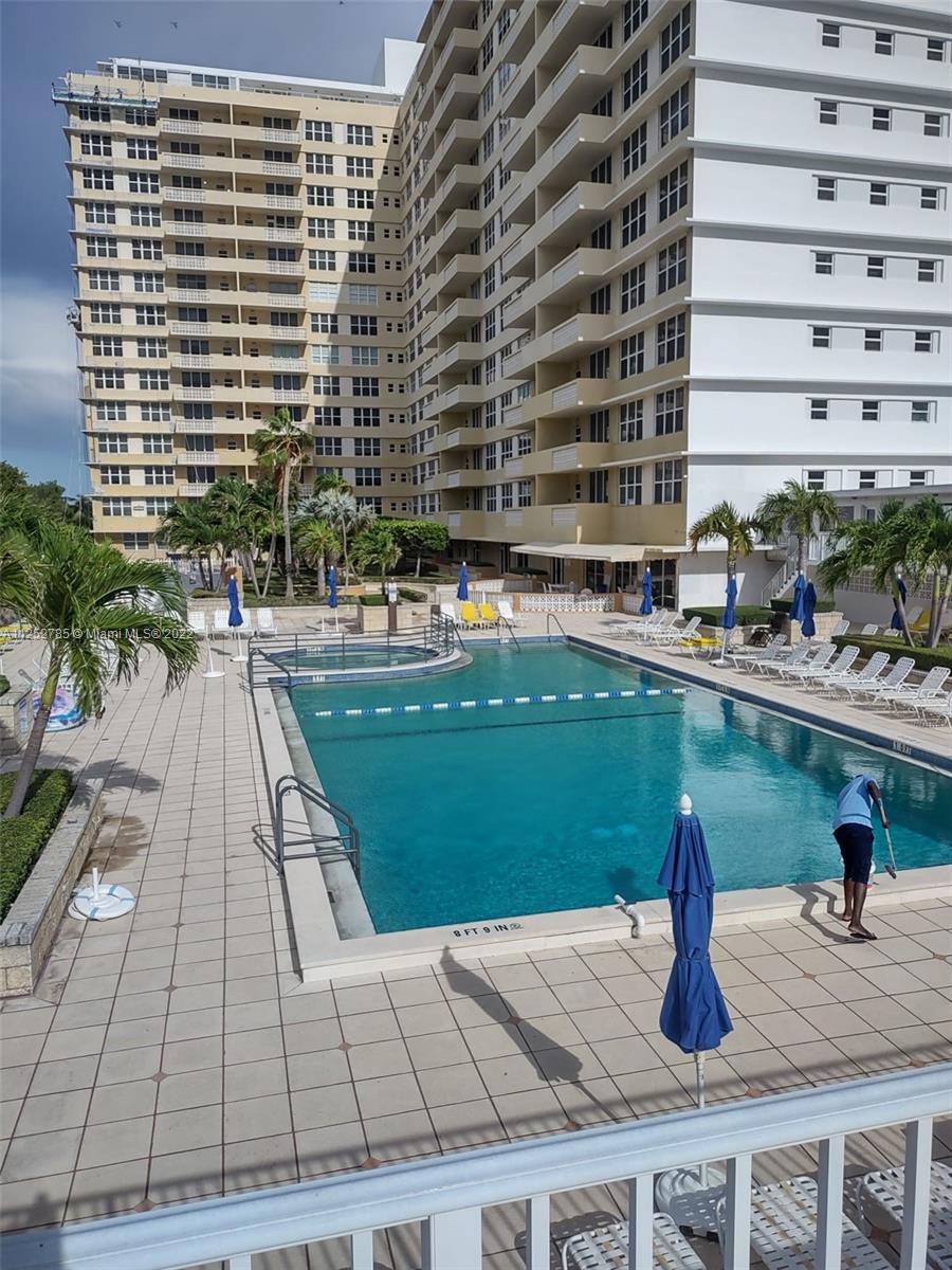 An outdoor swimming pool area with lounge chairs and a tall apartment building in the background — 4747 Collins Ave # 107, Miami Beach FL 33140, MIAMI BEACH, FL