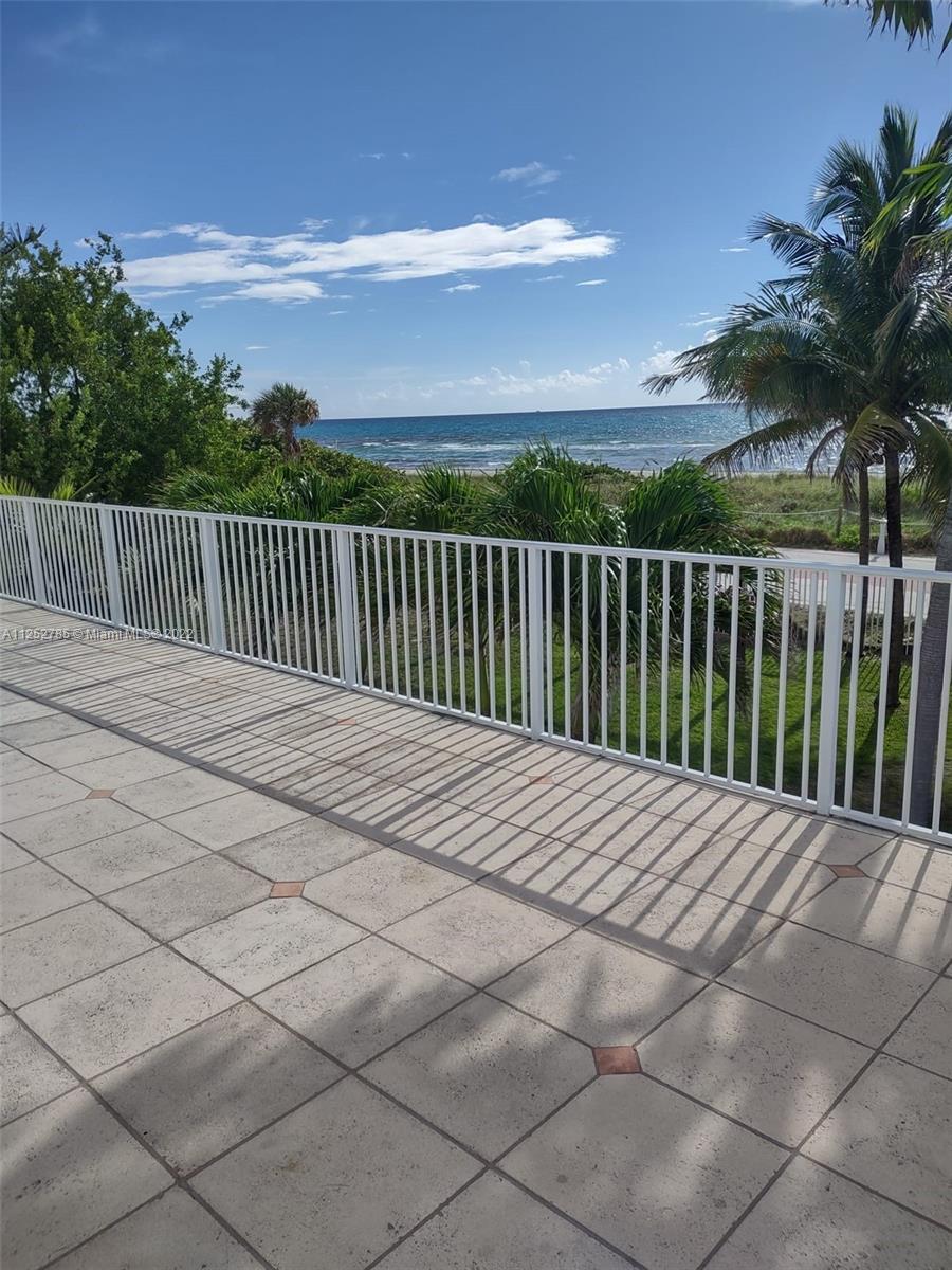 A tiled balcony with a white railing overlooks palm trees and the ocean — 4747 Collins Ave # 107, Miami Beach FL 33140, MIAMI BEACH, FL