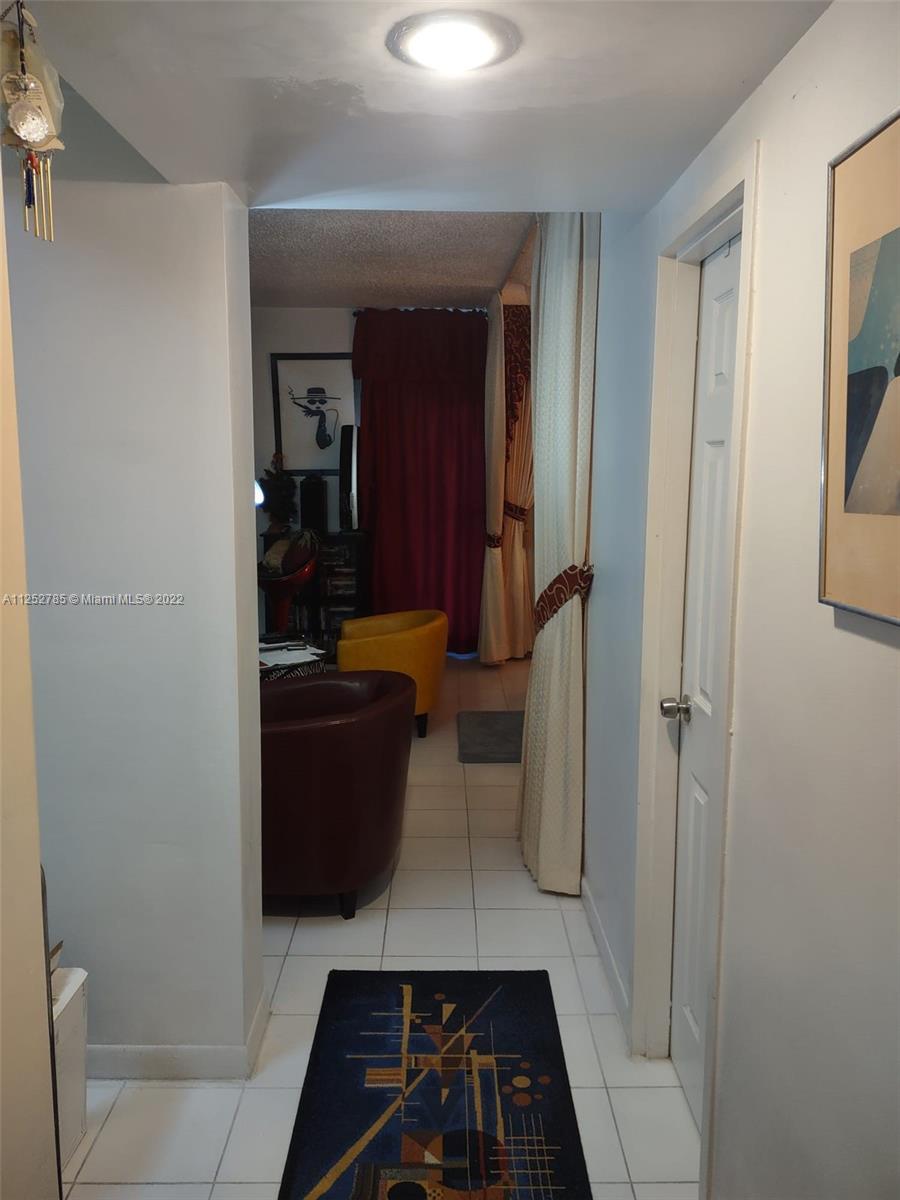 A hallway with white tile floors leads into a living area with two armchairs — 4747 Collins Ave # 107, Miami Beach FL 33140, MIAMI BEACH, FL