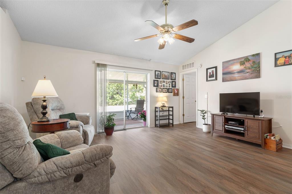 A living room features wood-look flooring, a ceiling fan, a television console, and sliding doors — 38 LLOYD TRAIL, PALM COAST, FL