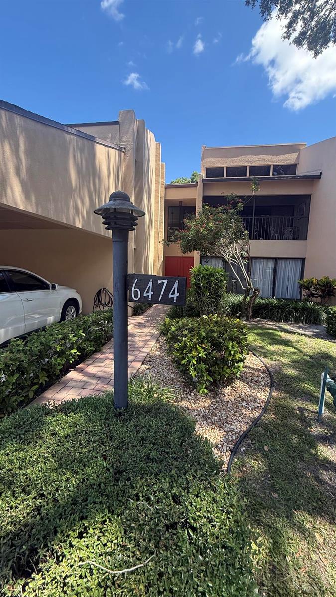 A two-story tan stucco building features a covered walkway, a numbered post, and landscaping — 6474 Pumpkin Seed Circle # 206, Boca Raton FL 33433, BOCA RATON, FL
