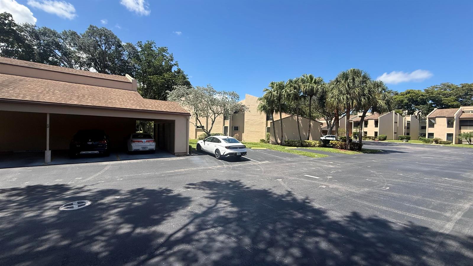 A parking lot with a covered carport and multi-story apartment buildings under a blue sky — 6474 Pumpkin Seed Circle # 206, Boca Raton FL 33433, BOCA RATON, FL