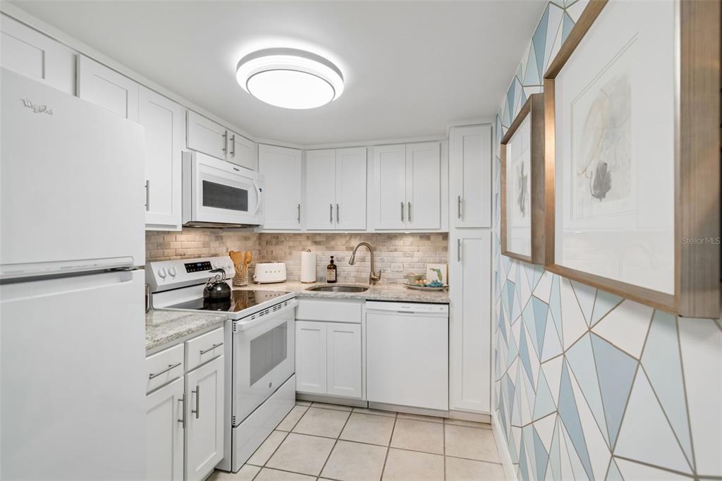 A white kitchen features light cabinetry, granite countertops, a tiled backsplash, and geometric patterned wallpaper — 4015 BAYSHORE BOULEVARD UNIT 7D, TAMPA, FL