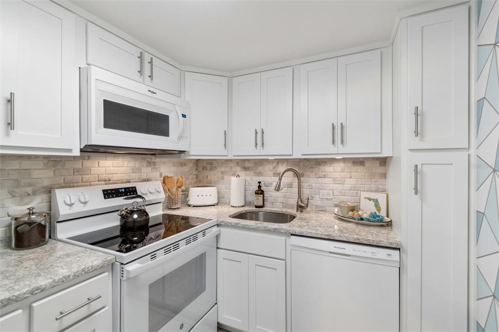 A white kitchen features granite countertops, a subway tile backsplash, and stainless steel appliances — 4015 BAYSHORE BOULEVARD UNIT 7D, TAMPA, FL