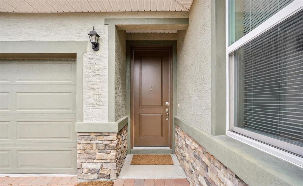 A brown front door is set in a stucco and stone exterior next to a garage — 5255 NW 33RD PLACE, OCALA, FL