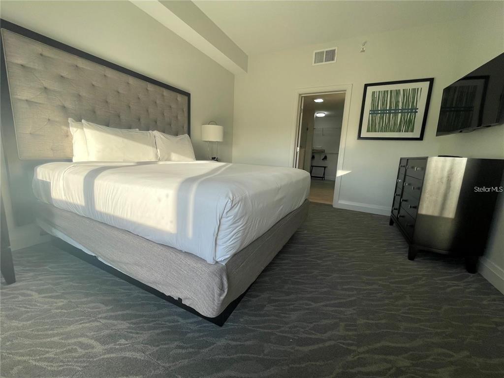 A bedroom features a tufted headboard, a white bed, a dark dresser, and patterned carpet — 14501 GROVE RESORT AVENUE, WINTER GARDEN, FL