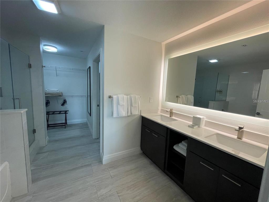 A modern bathroom features a double vanity with a backlit mirror and an adjacent walk-in closet — 14501 GROVE RESORT AVENUE, WINTER GARDEN, FL