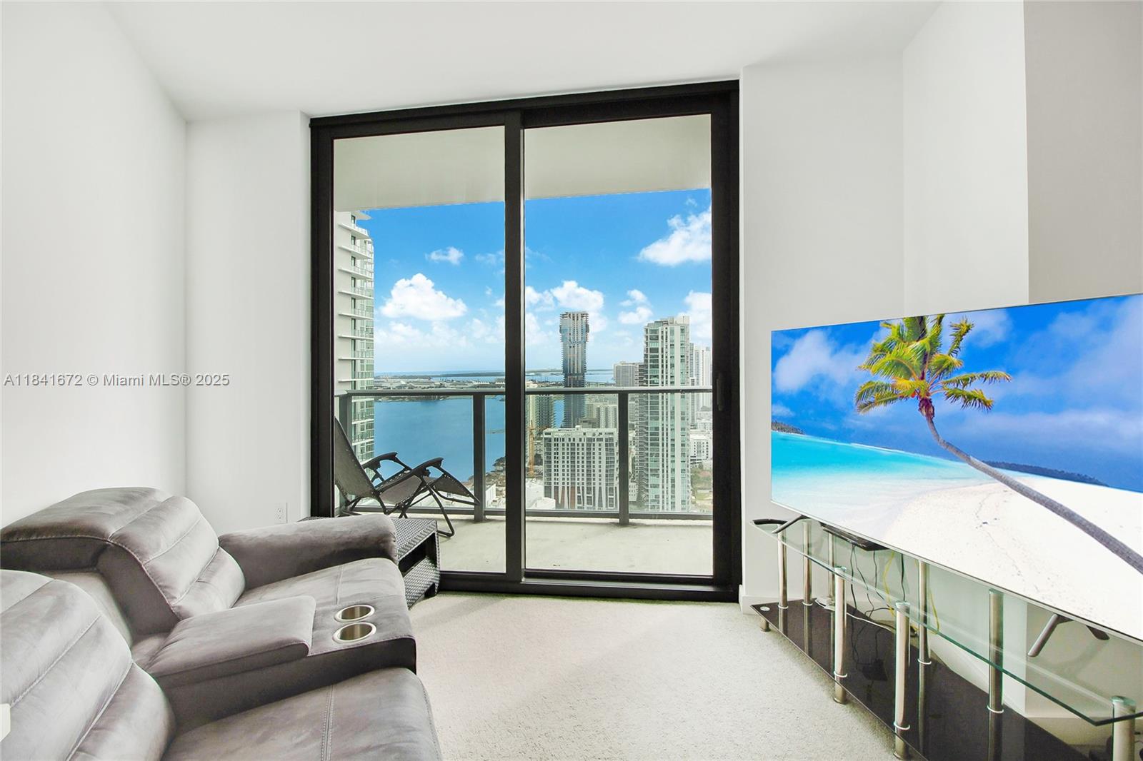 A living room features a grey sofa, a glass TV stand, and a balcony with water views — 501 NE 31st St # 3607, Miami FL 33137, MIAMI, FL