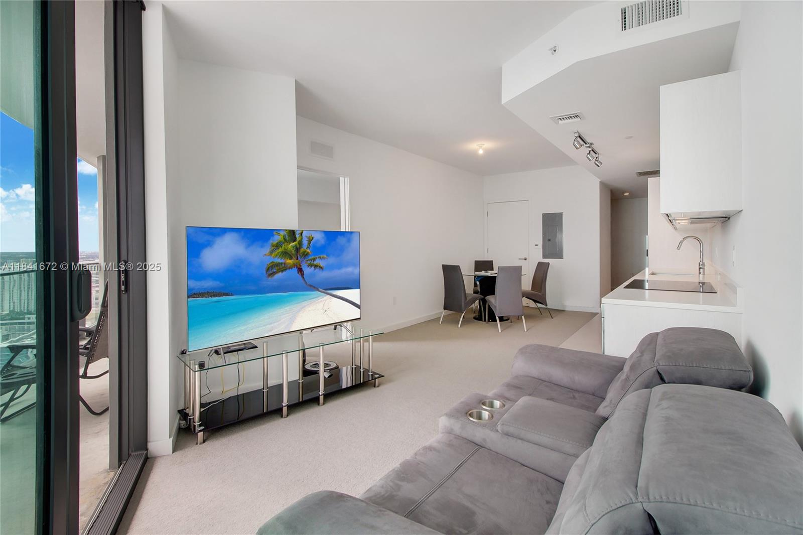 A modern living room features a gray sofa, a television on a glass stand, and a dining area — 501 NE 31st St # 3607, Miami FL 33137, MIAMI, FL