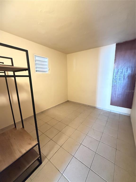 A small, empty room with light-colored tile flooring, beige walls, a louvered window, and a door — Bo.Palmas CALLE CUCHARILLAS UNIT 228, CATANO, PR