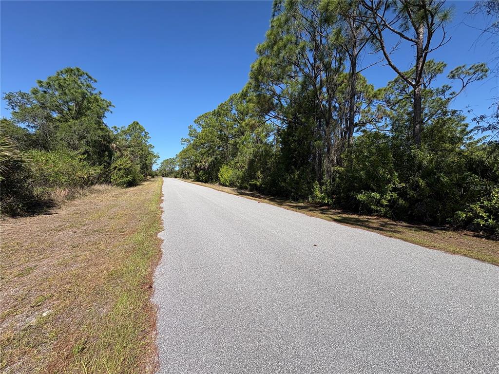 A paved road stretches through a wooded area under a clear blue sky — 14060 KLEFF AVENUE, PORT CHARLOTTE, FL