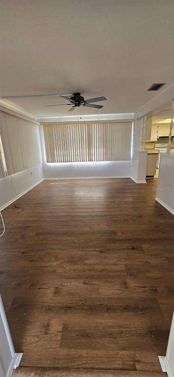 An empty room features wood-look flooring, a ceiling fan, and large windows with vertical blinds — 3602 HARBOR BOULEVARD, PORT CHARLOTTE, FL