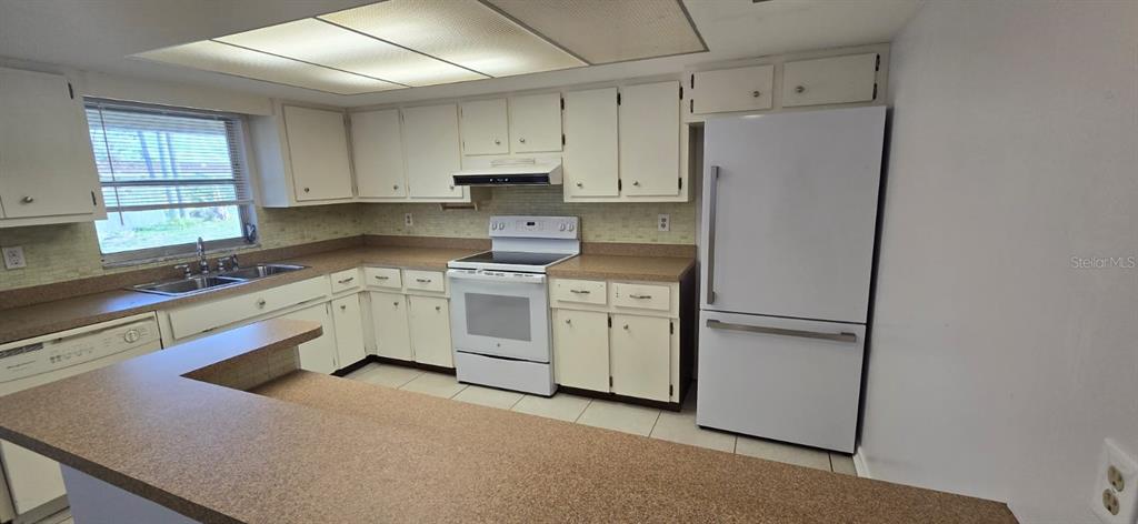 A kitchen features white cabinets, tan laminate countertops, white appliances, and a breakfast bar — 3602 HARBOR BOULEVARD, PORT CHARLOTTE, FL