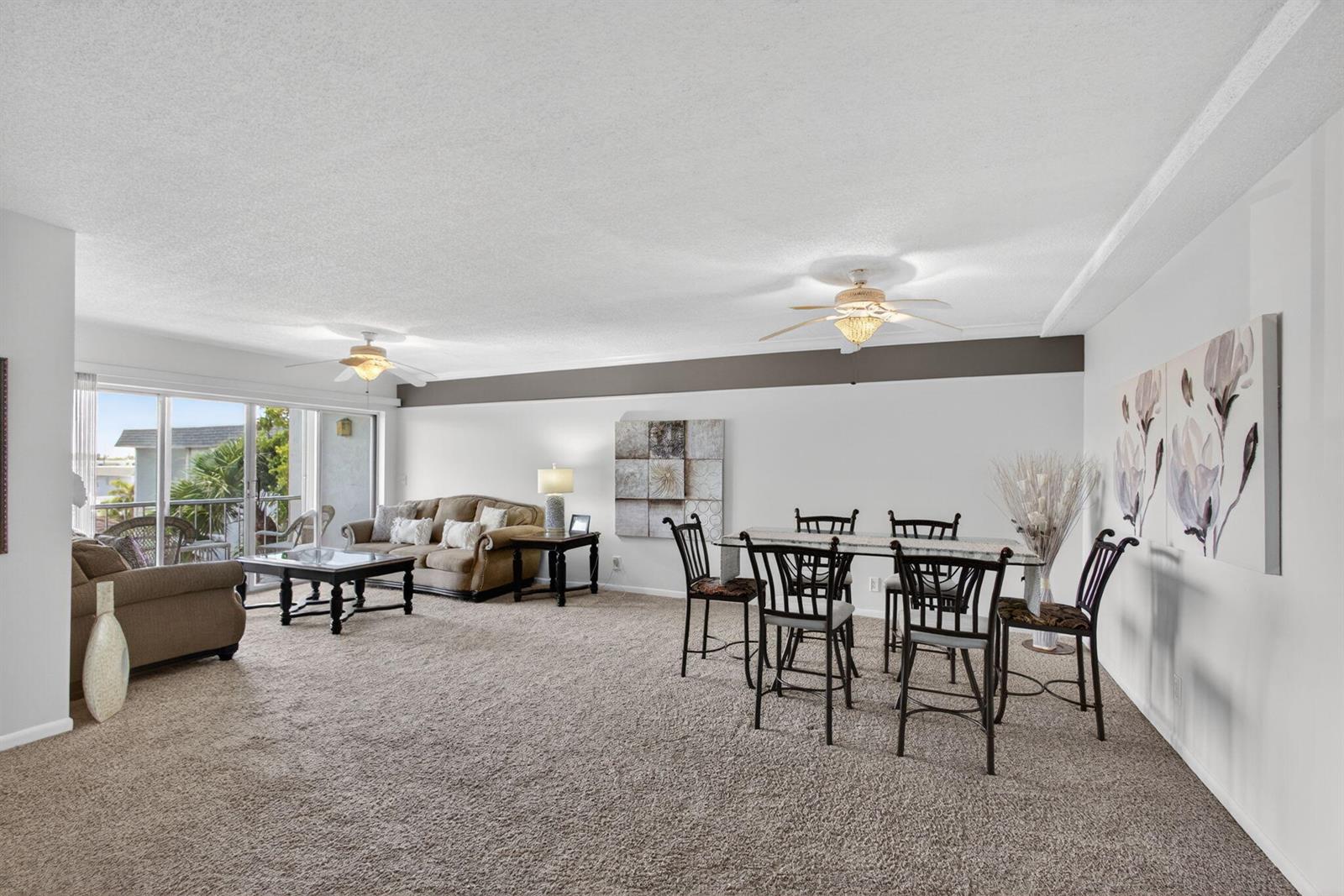 A living and dining area features beige carpeting, two ceiling fans, and a sliding glass door — 505 Spencer Drive # 211, West Palm Beach FL 33409, WEST PALM BEACH, FL