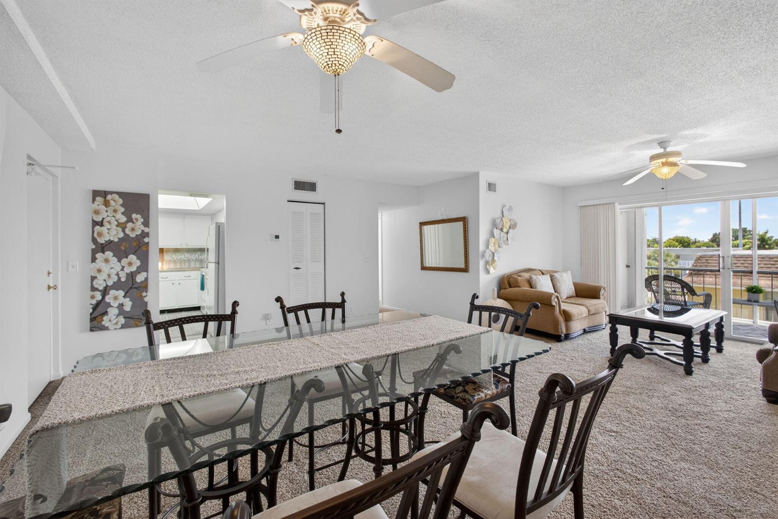 A dining area with a glass table and chairs opens into a carpeted living room — 505 Spencer Drive # 211, West Palm Beach FL 33409, WEST PALM BEACH, FL