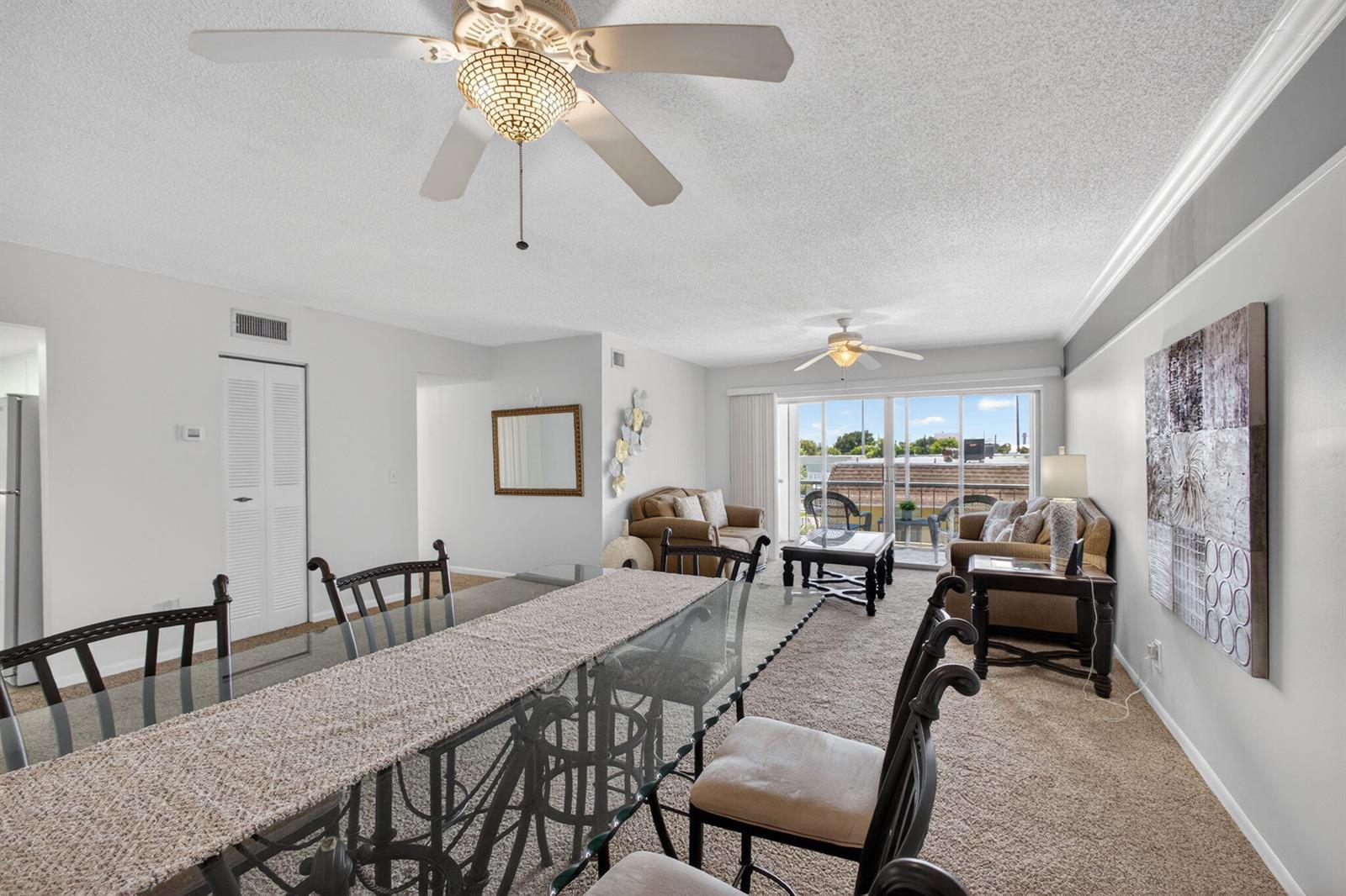 A living and dining area features a glass table, carpeted floors, and a sliding glass door — 505 Spencer Drive # 211, West Palm Beach FL 33409, WEST PALM BEACH, FL