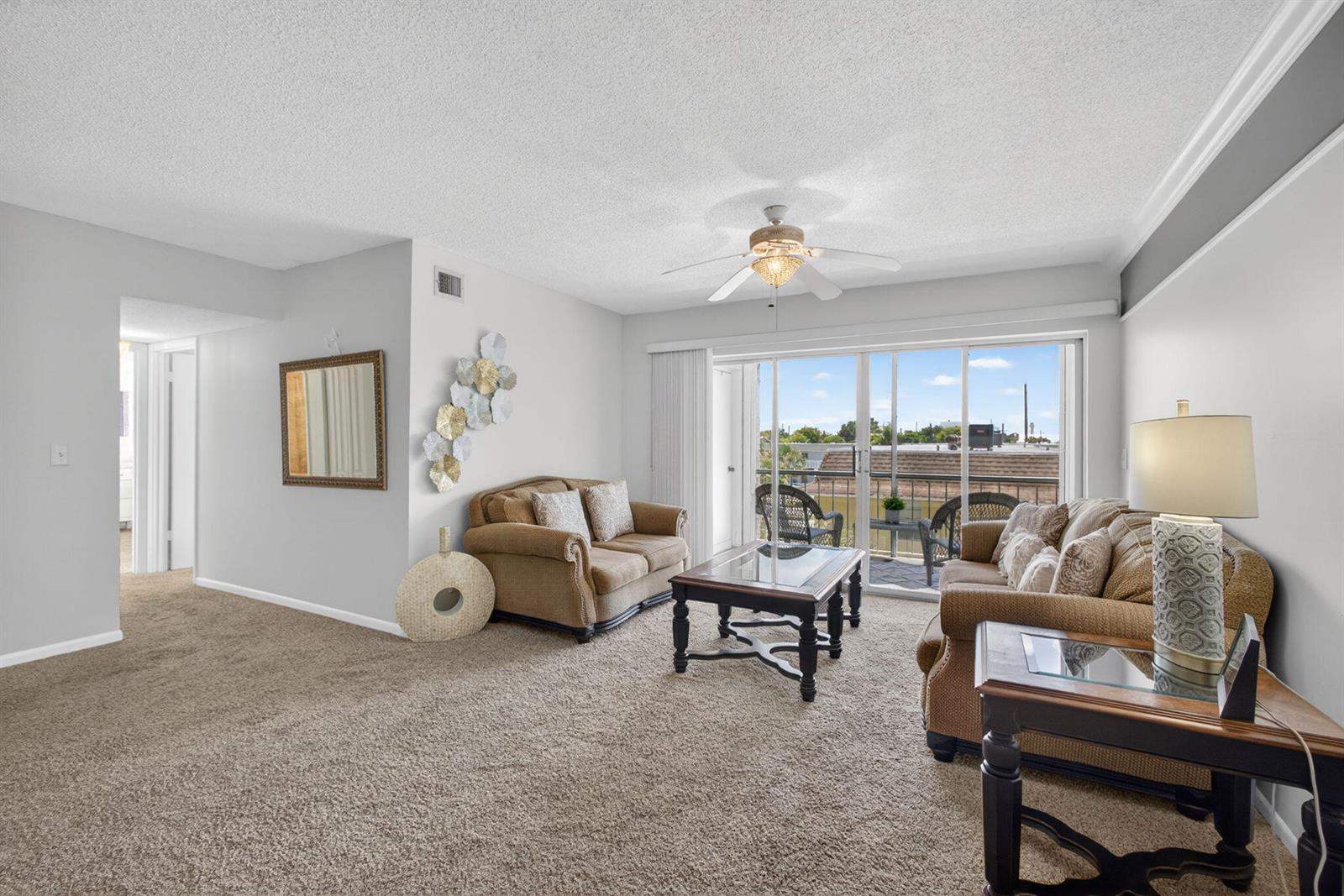 A living room features beige carpet, two brown sofas, a coffee table, and a balcony — 505 Spencer Drive # 211, West Palm Beach FL 33409, WEST PALM BEACH, FL
