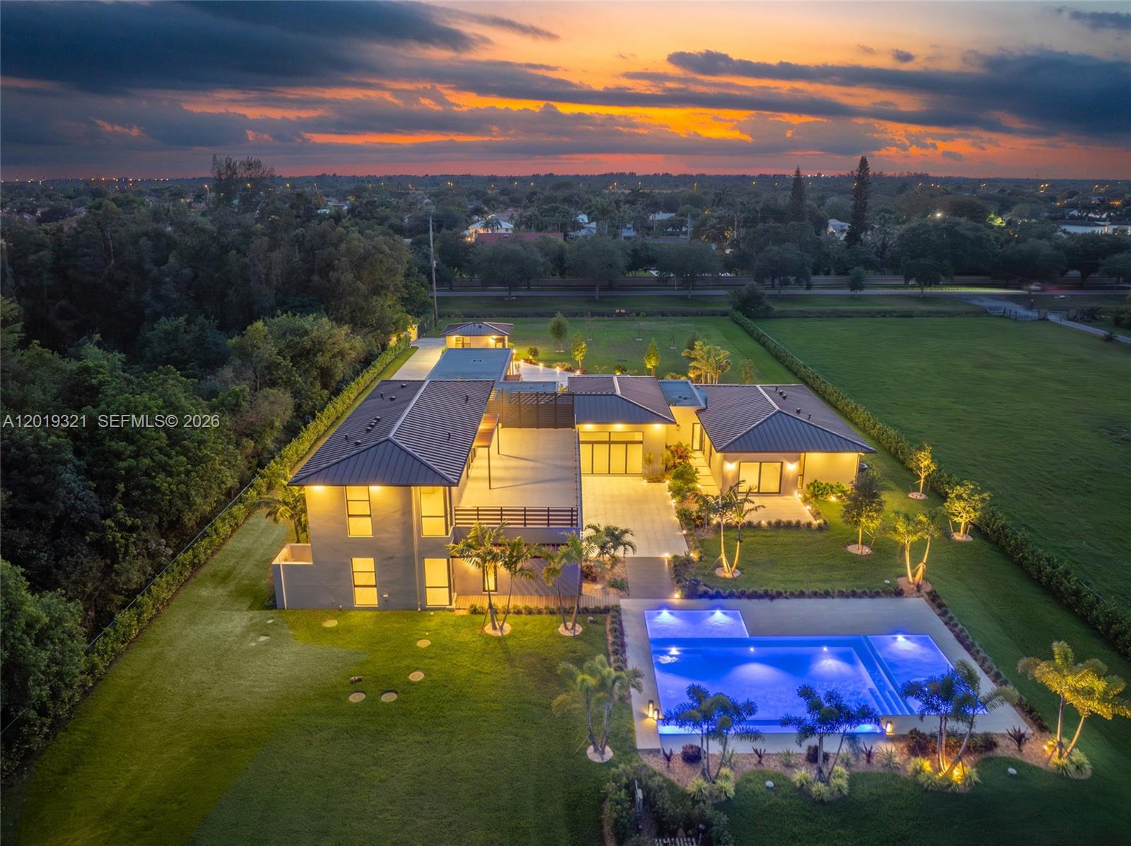 An aerial view shows a modern two-story house with a pool at sunset — 5500 SW 148th Ave, Southwest Ranches FL 33330, SOUTHWEST RANCHES, FL