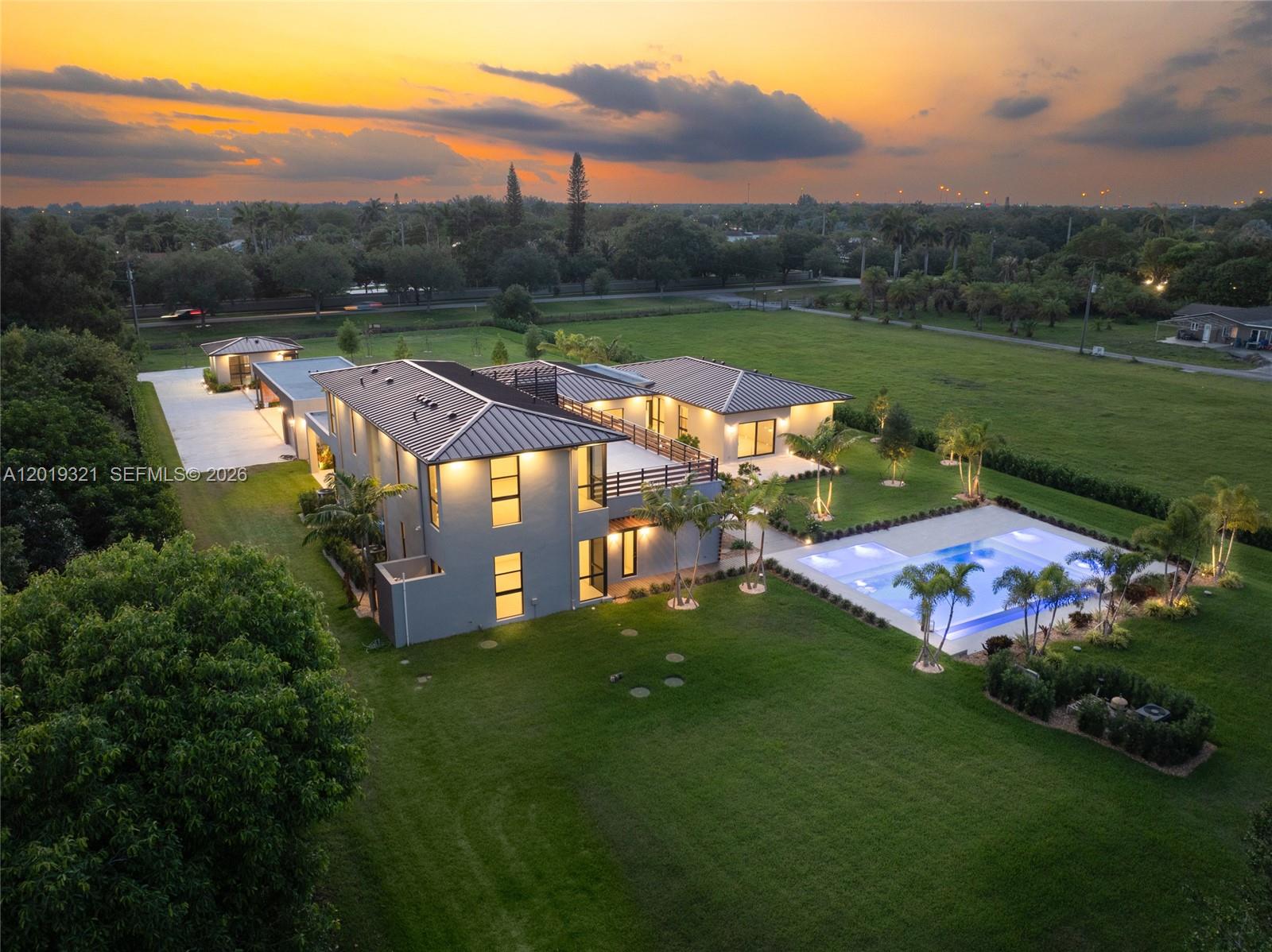 An aerial view shows a modern two-story house with a pool and large backyard at sunset — 5500 SW 148th Ave, Southwest Ranches FL 33330, SOUTHWEST RANCHES, FL