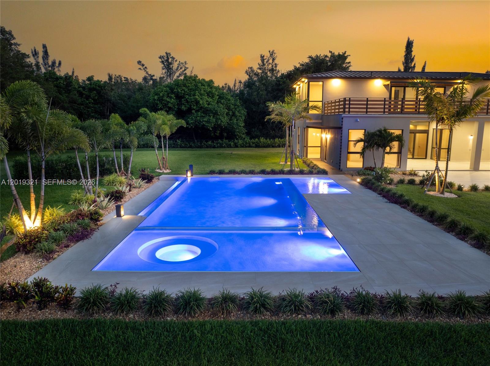 An illuminated rectangular swimming pool with a built-in circular spa sits beside a modern house — 5500 SW 148th Ave, Southwest Ranches FL 33330, SOUTHWEST RANCHES, FL