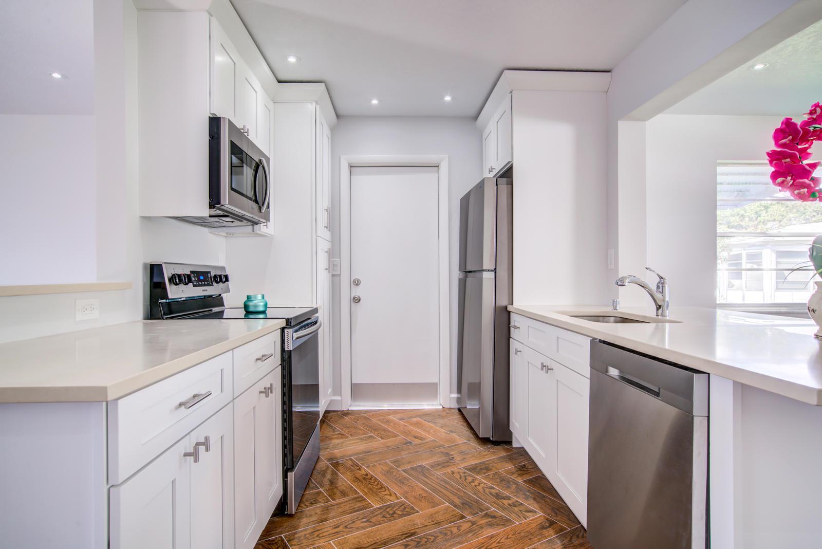 A modern kitchen features white cabinets, stainless steel appliances, quartz countertops, and herringbone wood flooring — 813 SW 5th Court, Boynton Beach FL 33426, BOYNTON BEACH, FL