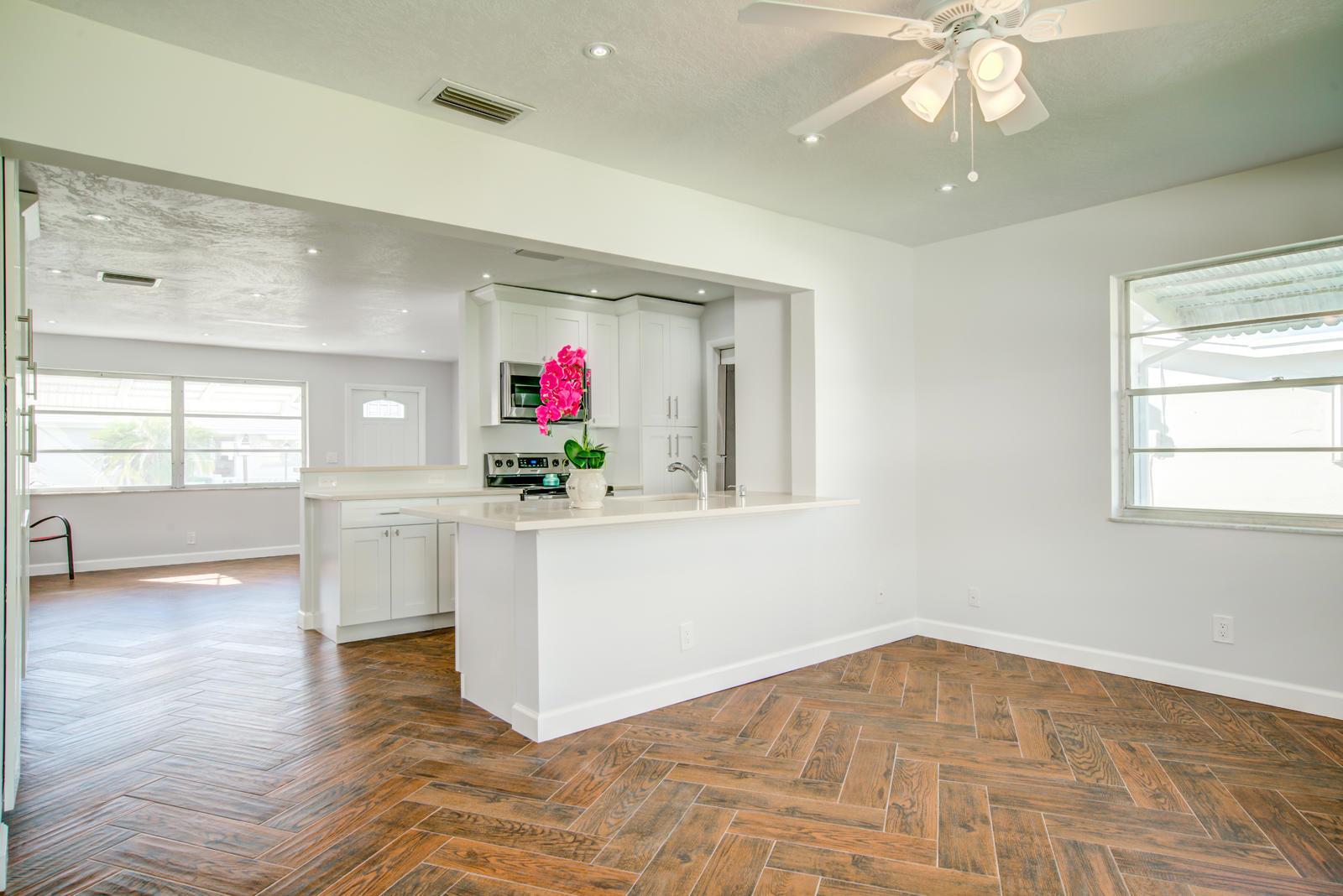 A kitchen with white cabinets and a peninsula overlooks a dining area with herringbone flooring — 813 SW 5th Court, Boynton Beach FL 33426, BOYNTON BEACH, FL