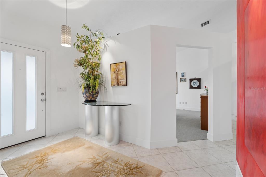A bright foyer features a glass-topped console table, a potted plant, and a beige rug — 4404 SIMMONS ROAD, ORLANDO, FL