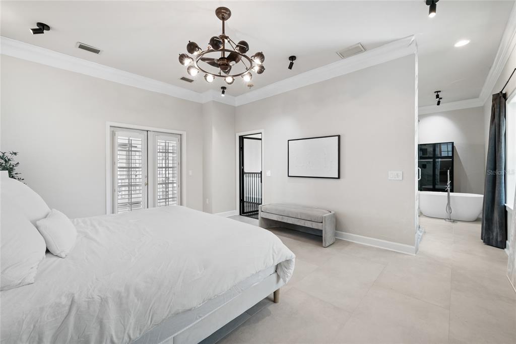 A bedroom with a white bed, chandelier, bench, and an open-concept bathroom with a tub — 5043 SW 91 DRIVE, GAINESVILLE, FL