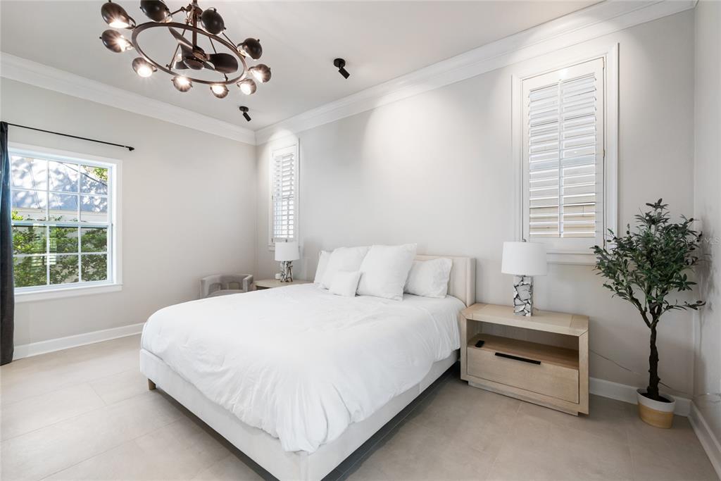 A bedroom features a white bed, two nightstands with lamps, and a modern chandelier — 5043 SW 91 DRIVE, GAINESVILLE, FL