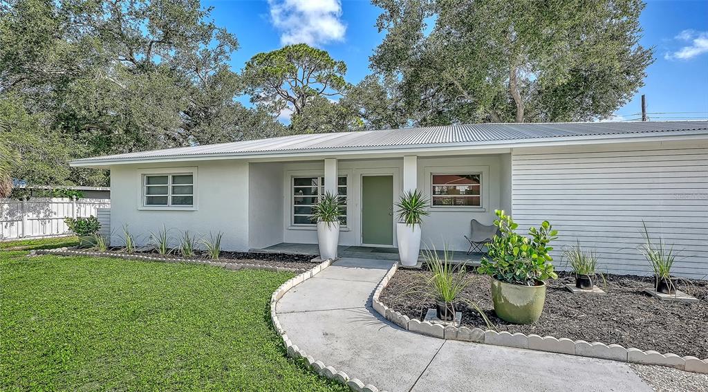 A white single-story house with a metal roof, a green front door, and landscaped yard — 2719 TEMPLE STREET, SARASOTA, FL