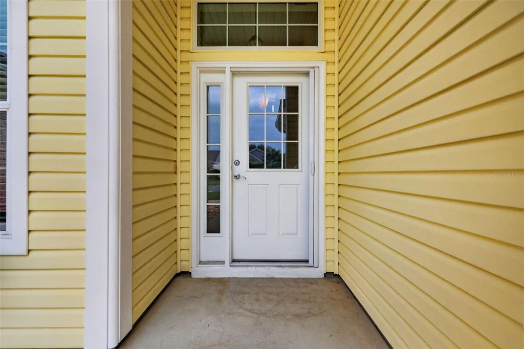 A white front door with a sidelight is set between yellow vinyl siding walls — 2234 WESTCHESTER WAY, THE VILLAGES, FL