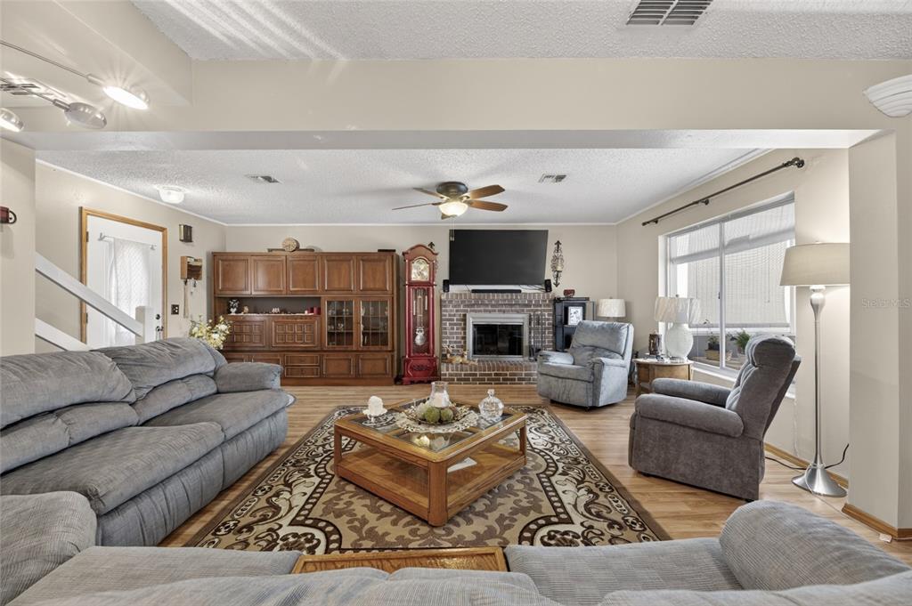 A living room features a brick fireplace, a large wooden hutch, and gray upholstered furniture — 3312 N LAKE DRIVE, PLANT CITY, FL