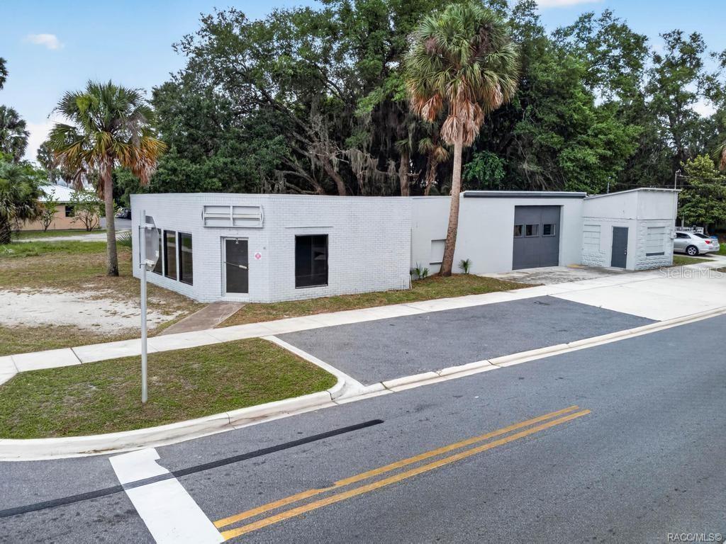 A white, single-story commercial building with a gray garage door and palm trees — 1321 SAINT JOHNS AVENUE, PALATKA, FL