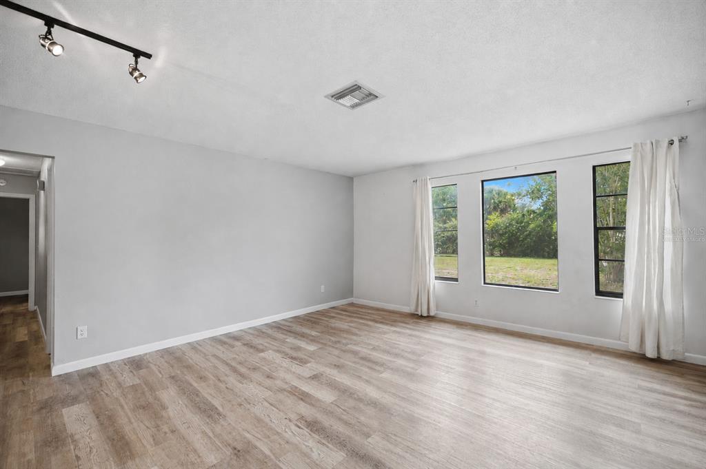 An empty room with light gray walls, wood-look flooring, track lighting, and three large windows — 477 SPRING LANE, OCALA, FL