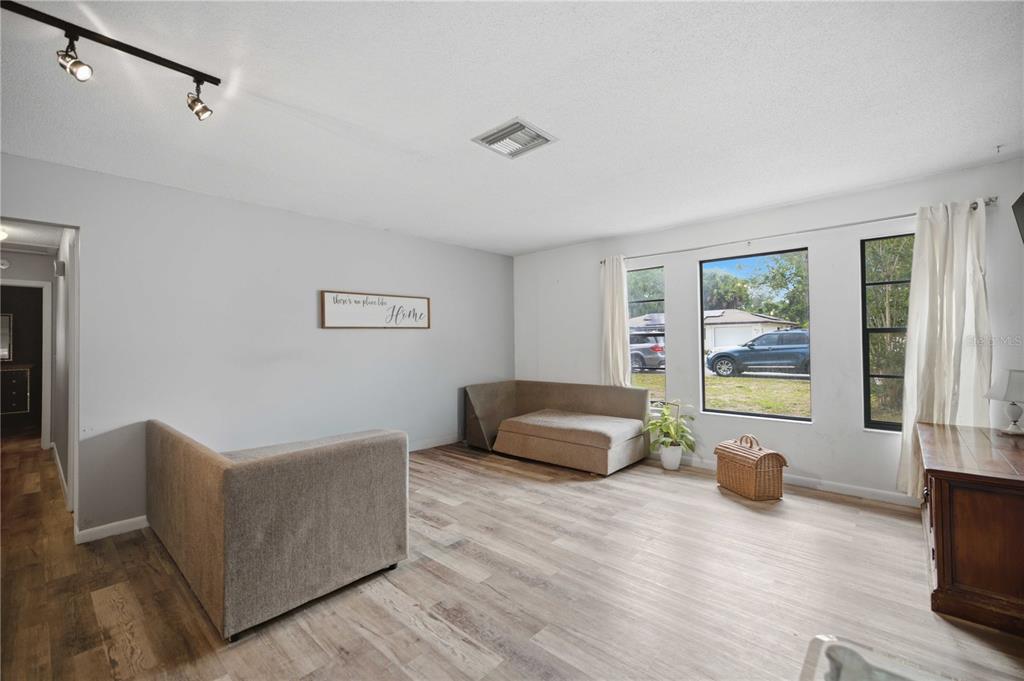 A living room with light wood-look flooring, gray walls, track lighting, and large windows — 477 SPRING LANE, OCALA, FL