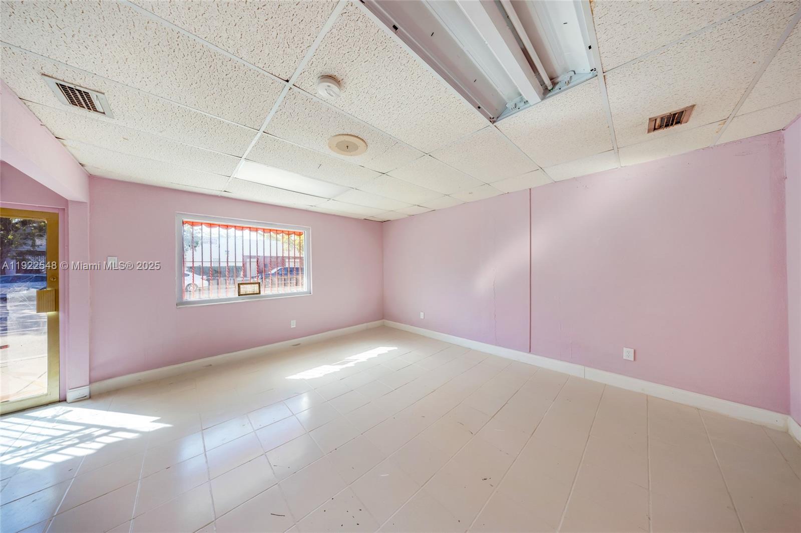 An empty room features pink walls, a drop ceiling, and light-colored tile flooring — 159 NW 36th St, Miami FL 33127, MIAMI, FL