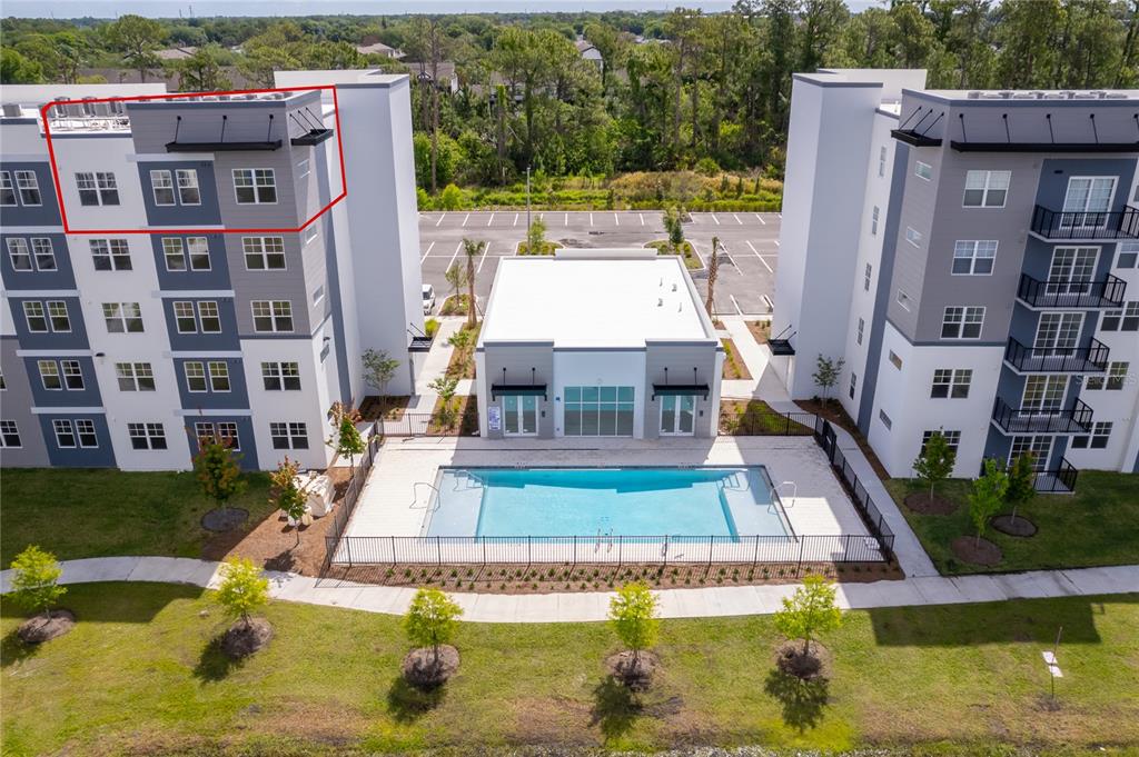 An aerial view shows a swimming pool between two modern apartment buildings with a parking lot — 5579 MILLENIA PARK BLVD UNIT 521, ORLANDO, FL