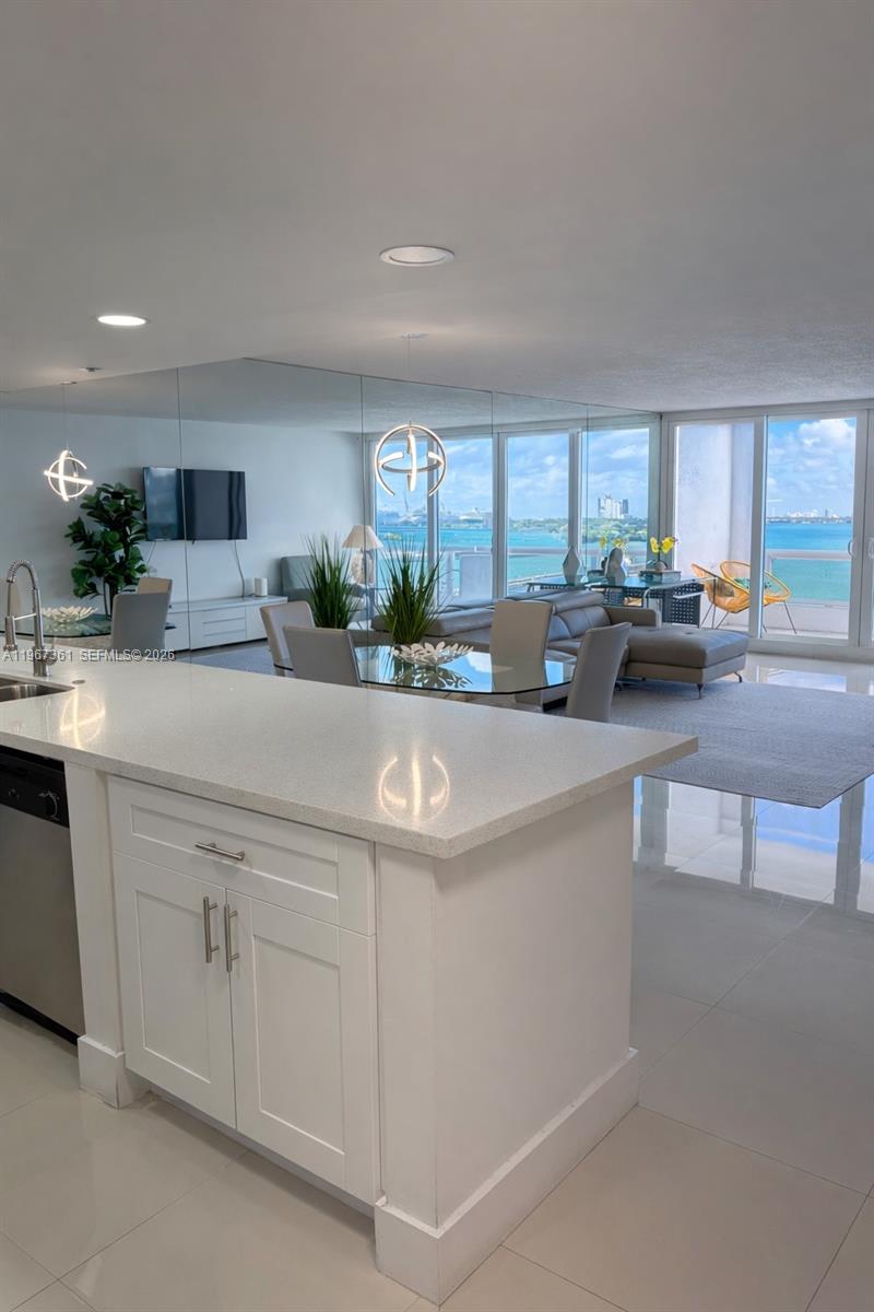 A modern kitchen island overlooks a dining area and living room with expansive ocean views — 1717 N Bayshore Dr # 1132, Miami FL 33132, MIAMI, FL
