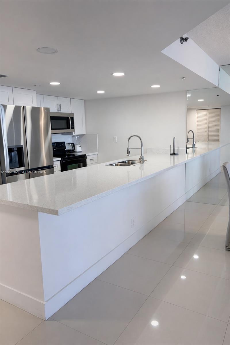 A modern kitchen features white cabinetry, stainless steel appliances, and a long quartz countertop island — 1717 N Bayshore Dr # 1132, Miami FL 33132, MIAMI, FL