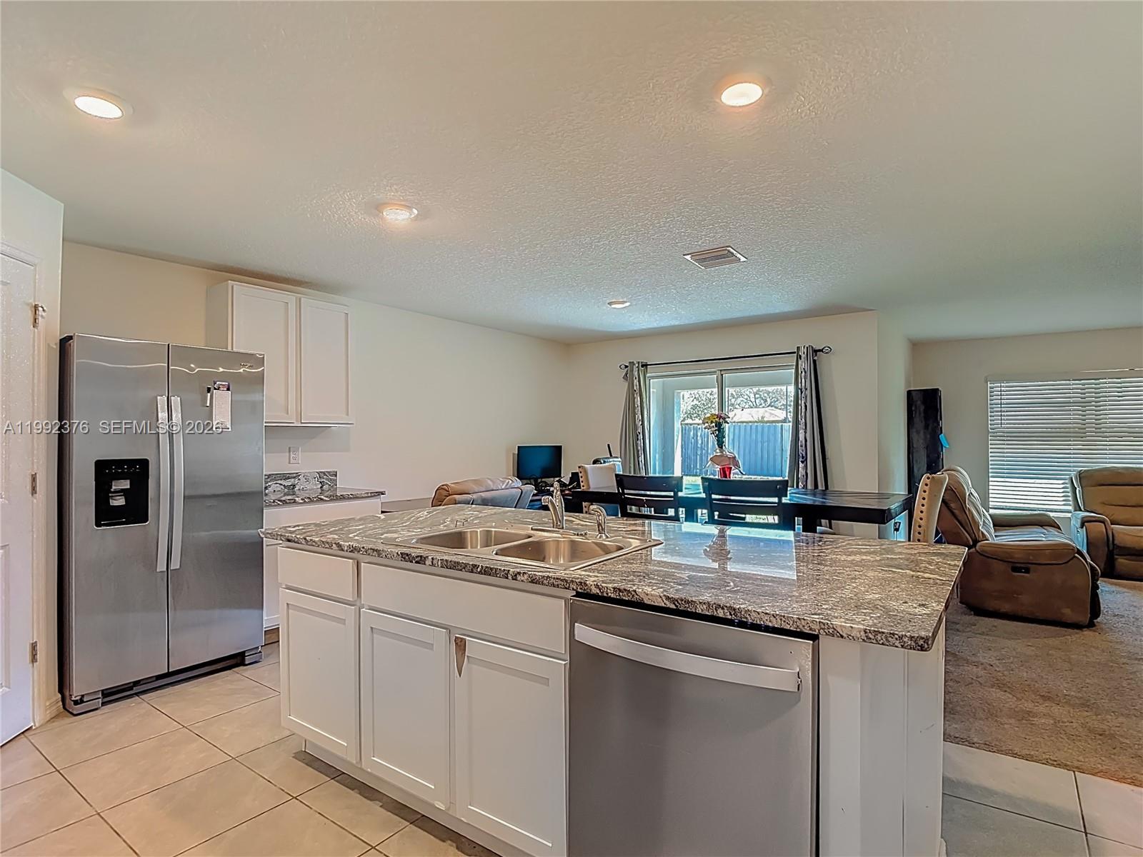 A kitchen features a granite-topped island with a sink, stainless steel appliances, and white cabinets — 3034 Rim Dr, Spring Hill FL 34609, SPRING HILL, FL