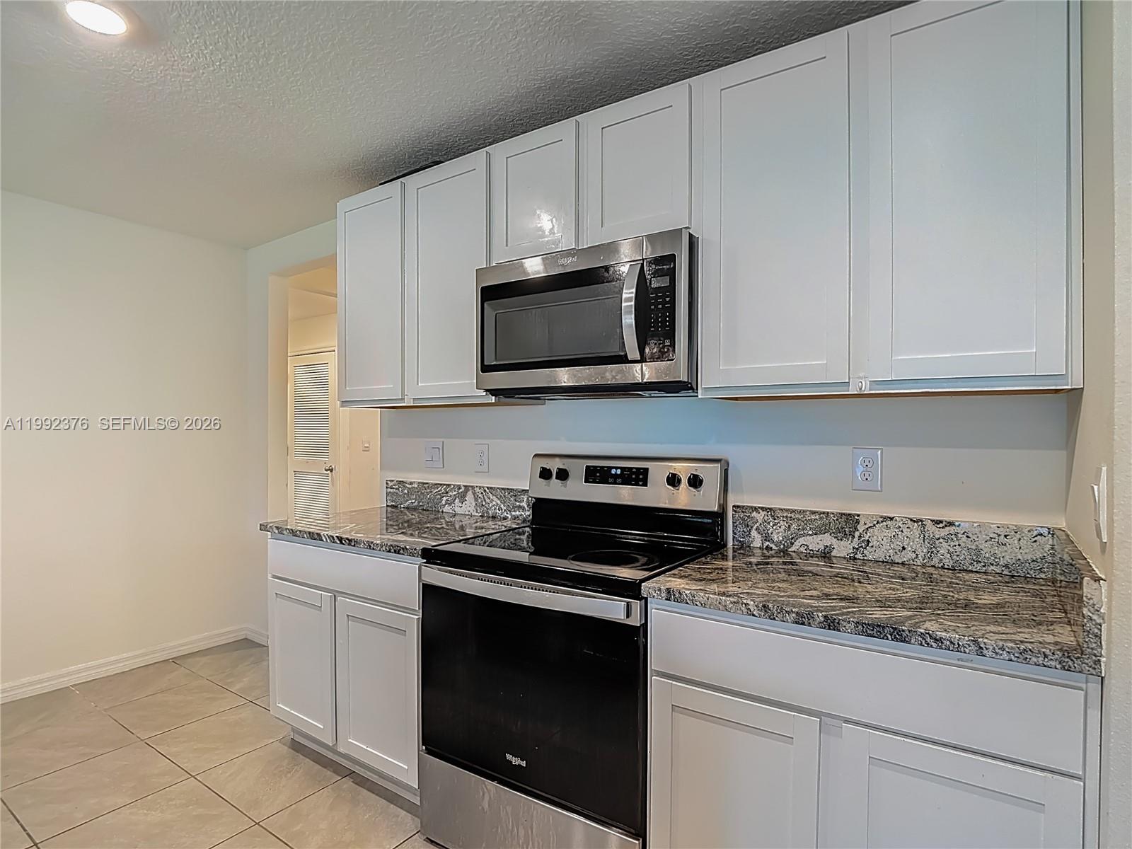 A kitchen features white cabinets, granite countertops, and stainless steel appliances — 3034 Rim Dr, Spring Hill FL 34609, SPRING HILL, FL