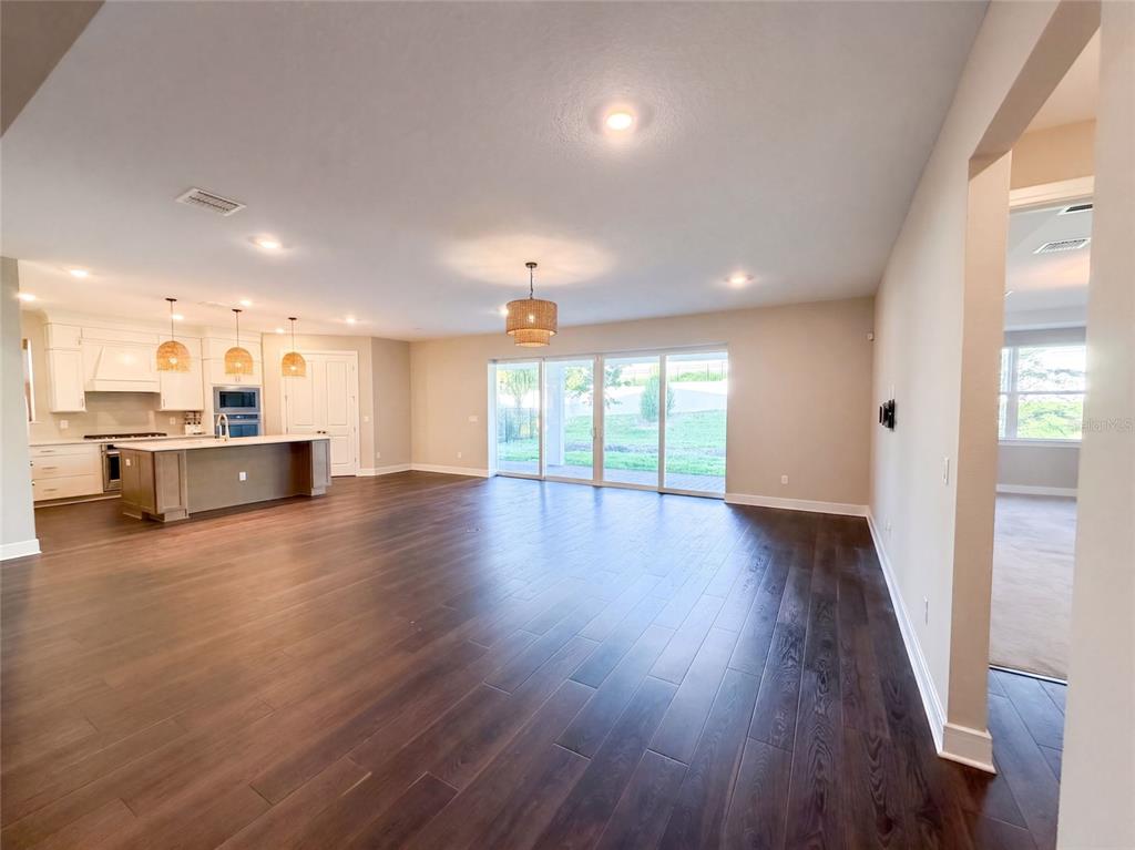 An open-concept kitchen and living area features dark wood flooring and large sliding glass doors — 15173 WILLOW RIDGE DRIVE, MONTVERDE, FL