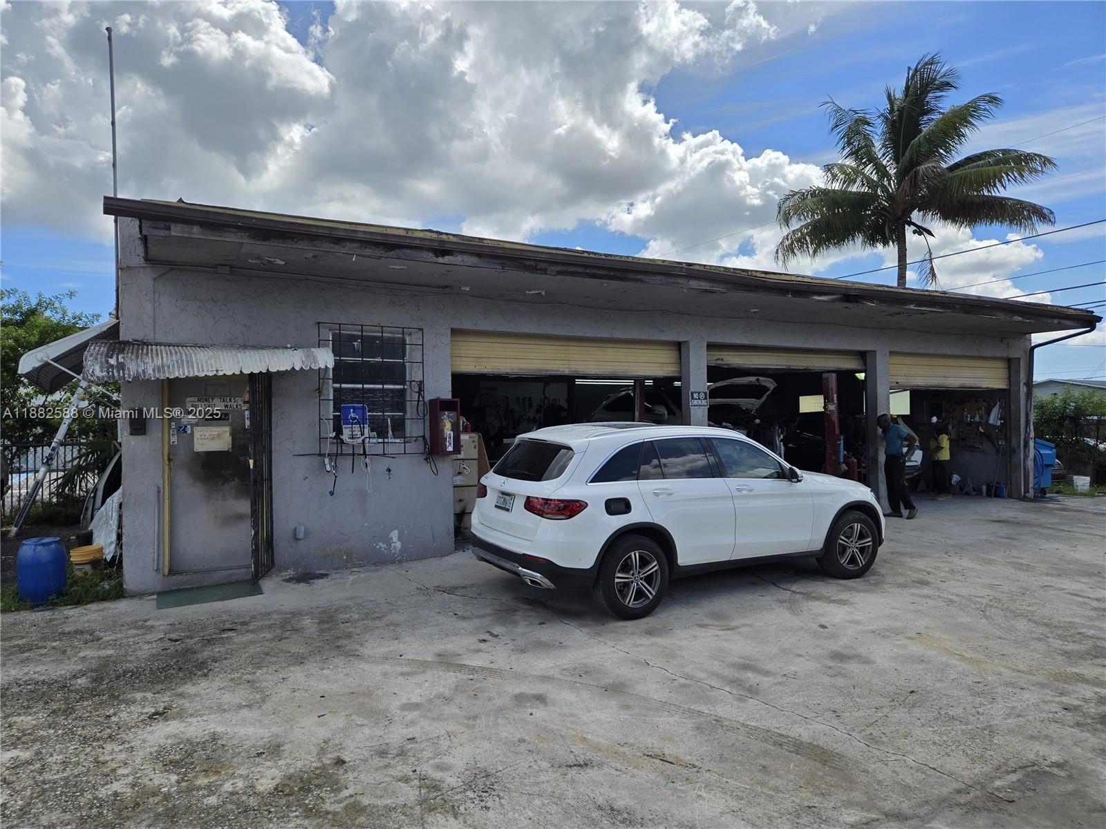 A white SUV is parked in front of a gray commercial garage with open bays — 5314 Pembroke Rd, West Park FL 33021, WEST PARK, FL
