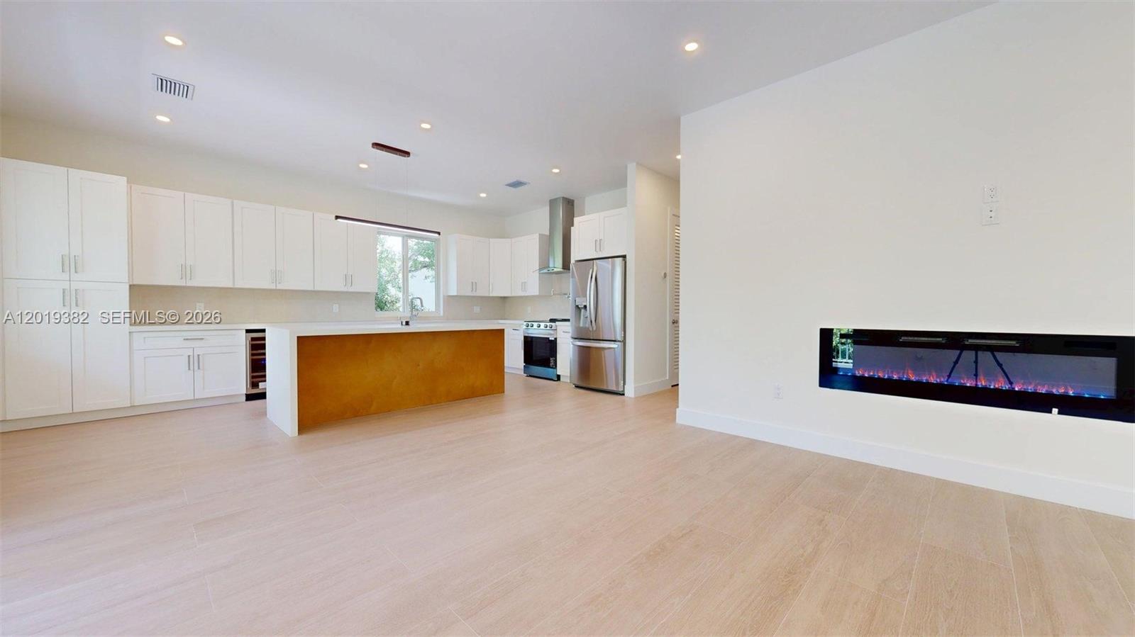A modern kitchen features white cabinetry, a wood-toned island, and a built-in electric fireplace — KEY LARGO, FL