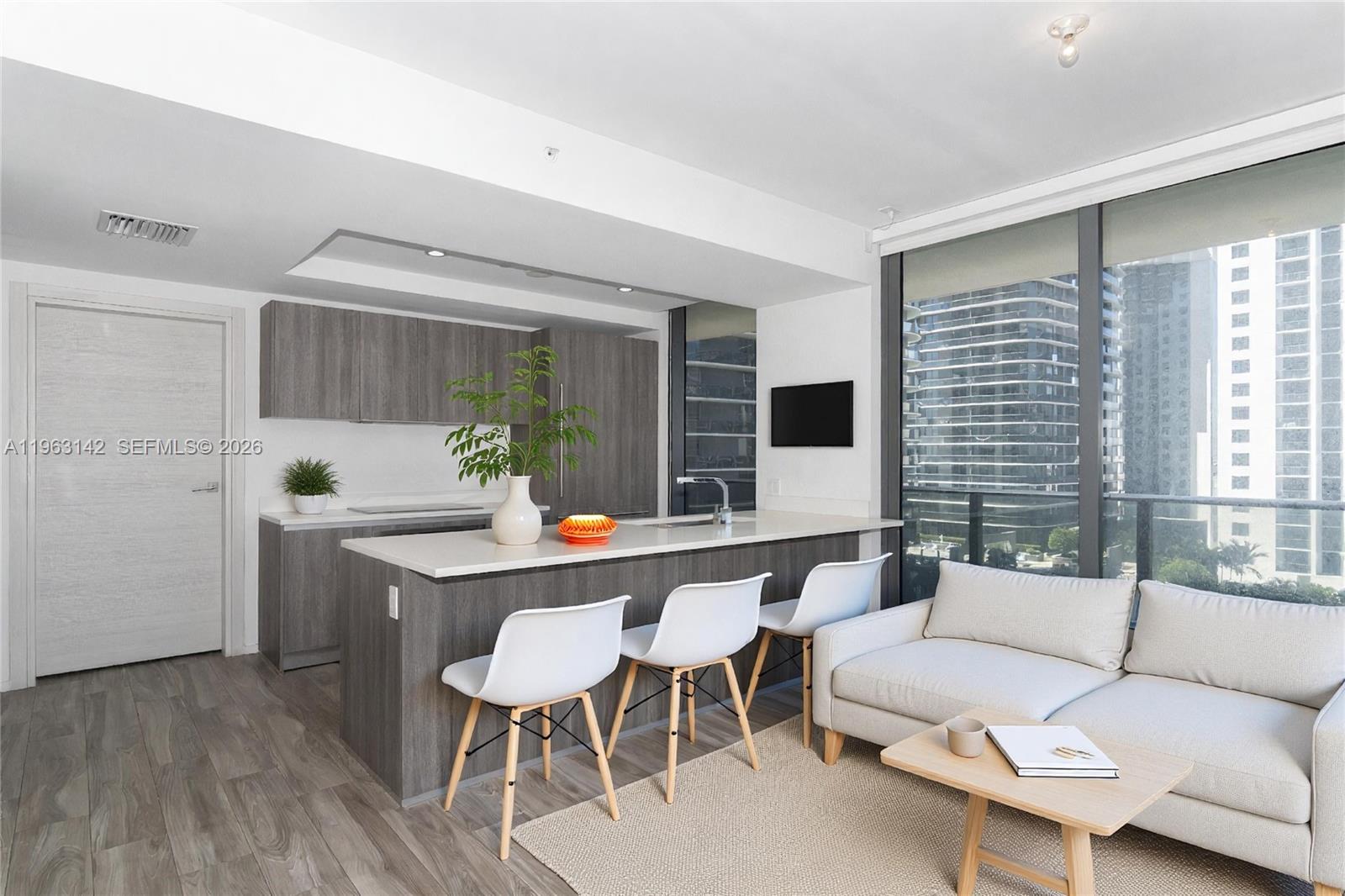 A modern kitchen with gray cabinetry and a white island sits beside a living area — 801 S Miami Ave # 1409, Miami FL 33130, MIAMI, FL