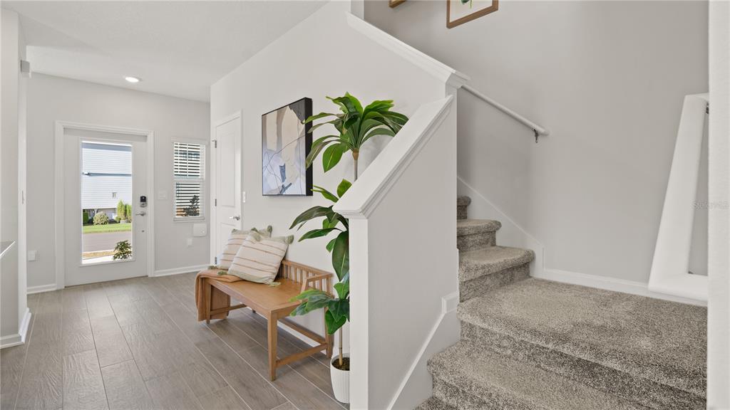 An entryway features a wooden bench, a potted plant, and carpeted stairs leading upward — 6067 WELLBEING WAY, CLERMONT, FL