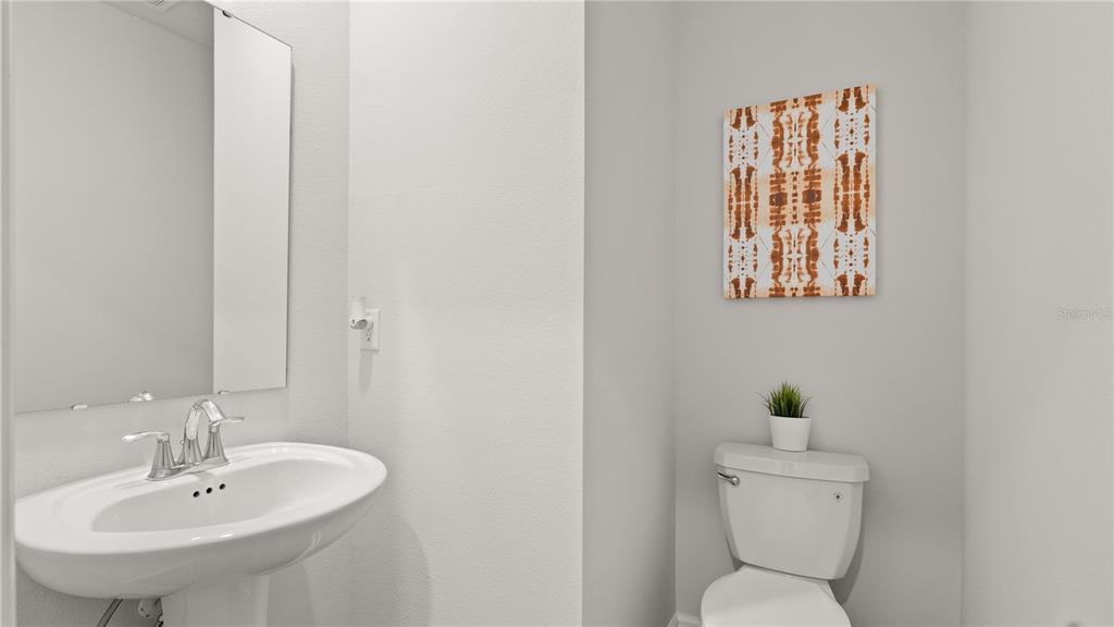 A half bathroom featuring a pedestal sink, a toilet with a small plant, and wall art — 6067 WELLBEING WAY, CLERMONT, FL