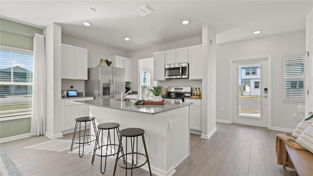 A modern kitchen features white cabinets, stainless steel appliances, a gray island, and tile flooring — 6067 WELLBEING WAY, CLERMONT, FL
