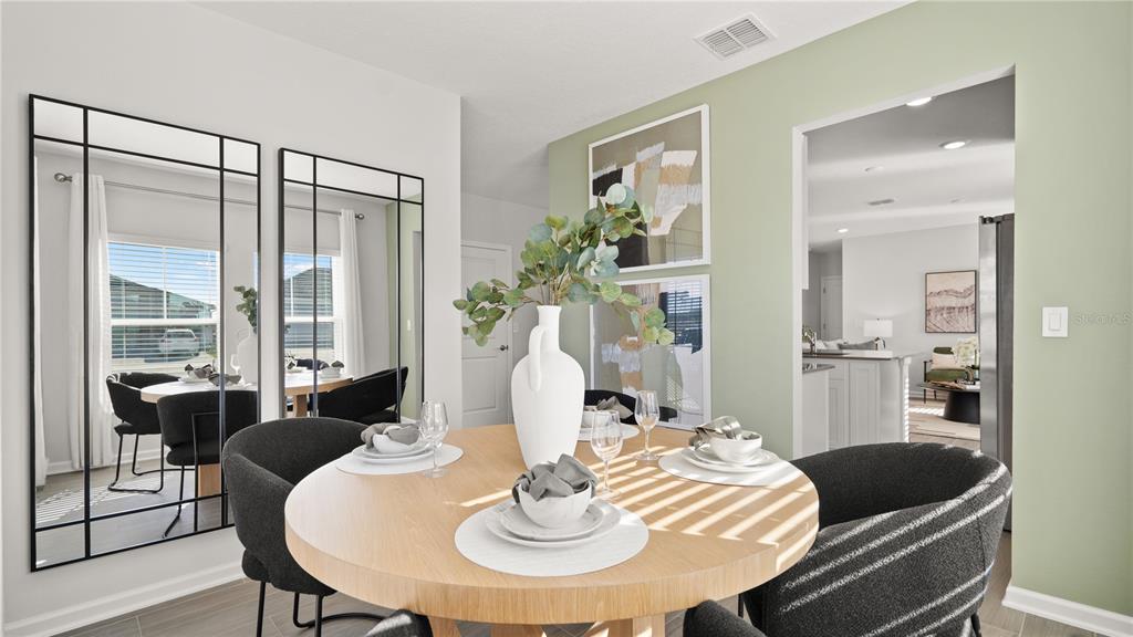 A dining area features a round wooden table, dark chairs, wall mirrors, and sage green walls — 6067 WELLBEING WAY, CLERMONT, FL