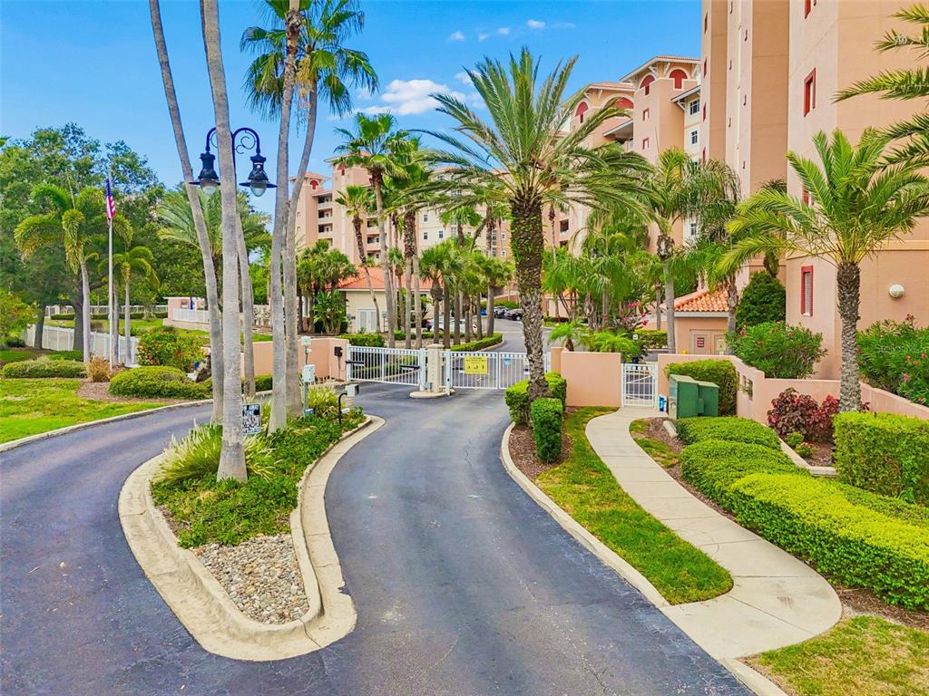 A gated entrance leads to a multi-story apartment building surrounded by palm trees and landscaping — 12033 GANDY BOULEVARD N UNIT 151, ST PETERSBURG, FL